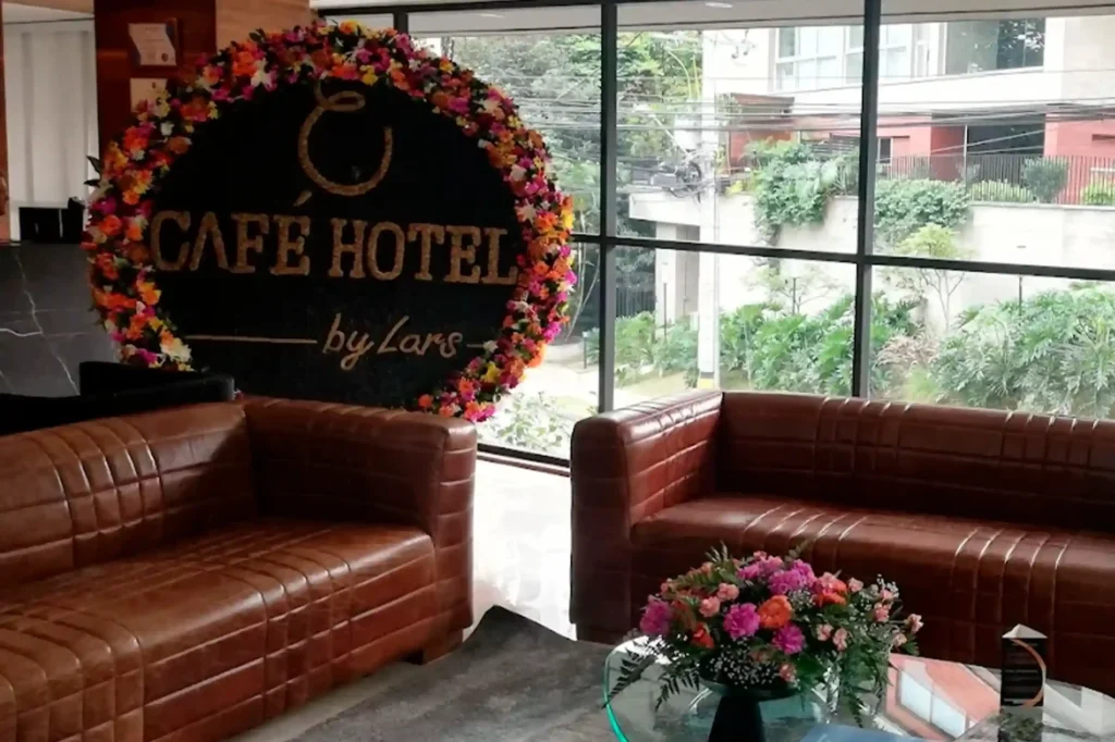 Lobby del Café Hotel by Lars en El Poblado con sofás de cuero marrón, arreglos florales y ventanales hacia la ciudad.