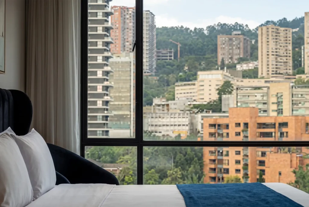 Habitación con cama king y vista panorámica al skyline residencial de El Poblado desde Café Hotel Medellín